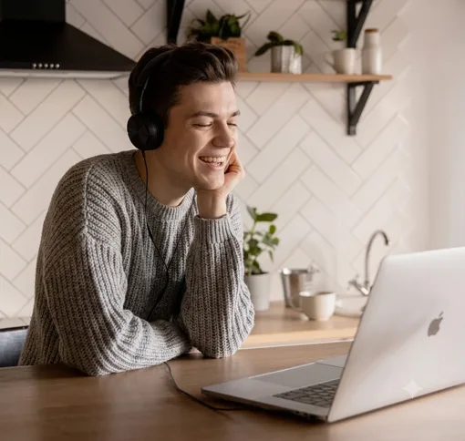 Smiling person wearing headphones on a video call at a kitchen table
